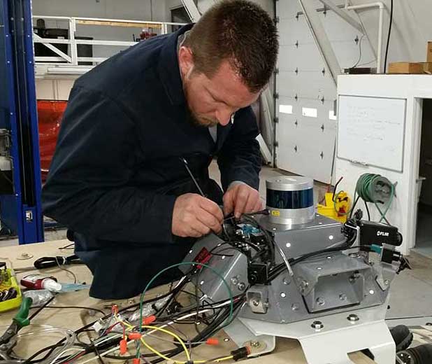 A technician in a laboratory at MTU installing an air and liquid cleaning system on a Lidar unit designed for military vehicles.